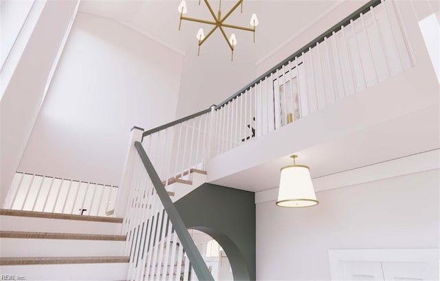 stairs with arched walkways, a notable chandelier, a towering ceiling, and crown molding