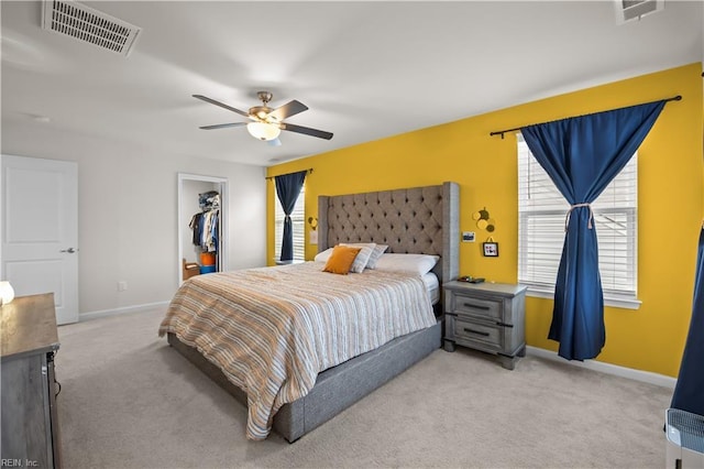 bedroom featuring visible vents, light colored carpet, a walk in closet, and baseboards