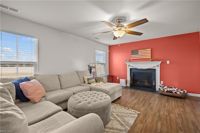 living room with visible vents, a glass covered fireplace, wood finished floors, baseboards, and ceiling fan