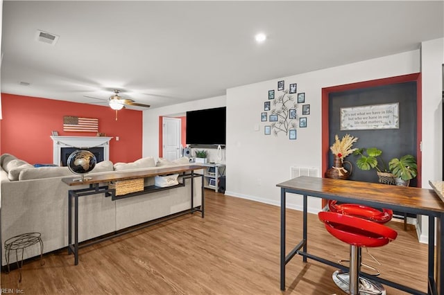 living area with wood finished floors, a ceiling fan, baseboards, visible vents, and a fireplace