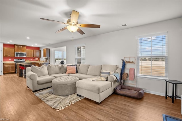 living area with light wood-type flooring, visible vents, a ceiling fan, recessed lighting, and baseboards