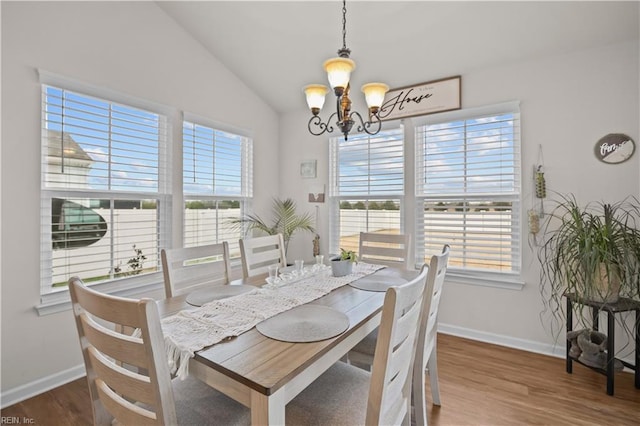 dining area with baseboards, wood finished floors, an inviting chandelier, and vaulted ceiling