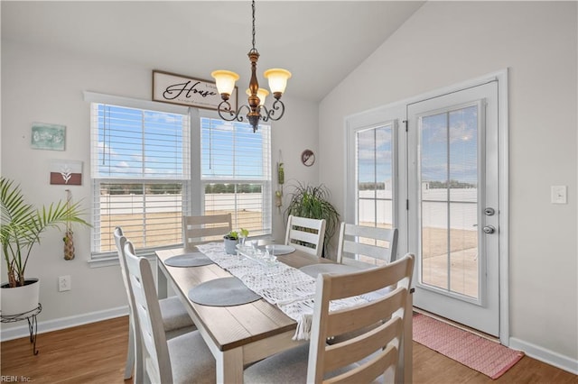 dining space with a notable chandelier, baseboards, lofted ceiling, and wood finished floors