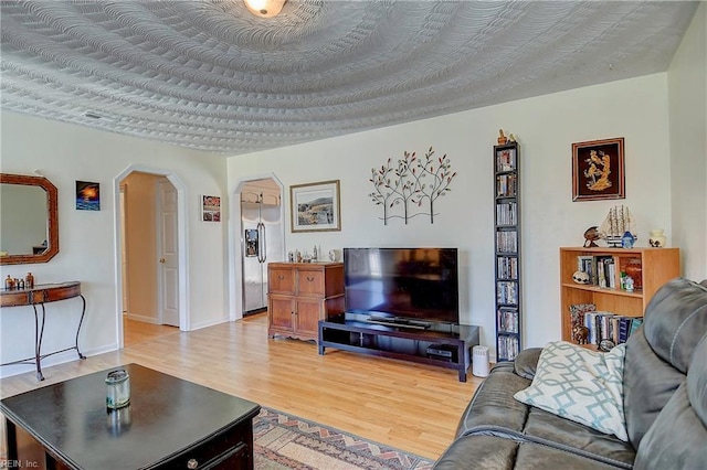 living room with light wood-style flooring, arched walkways, and a textured ceiling