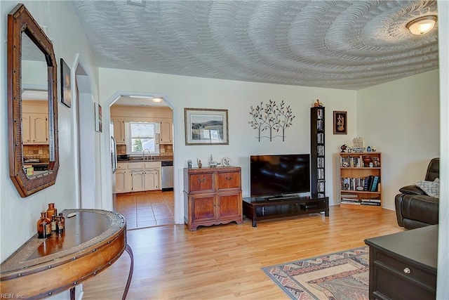 living room with arched walkways, light wood-style floors, and a textured ceiling