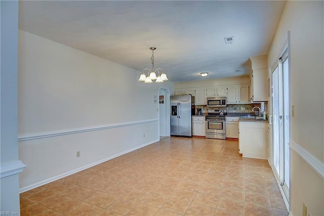 kitchen featuring a sink, stainless steel appliances, dark countertops, a notable chandelier, and backsplash