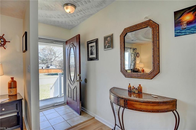 foyer with light tile patterned floors, a textured ceiling, and baseboards