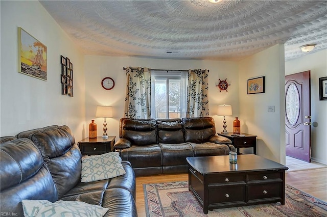 living room with light wood-type flooring, a textured ceiling, and visible vents