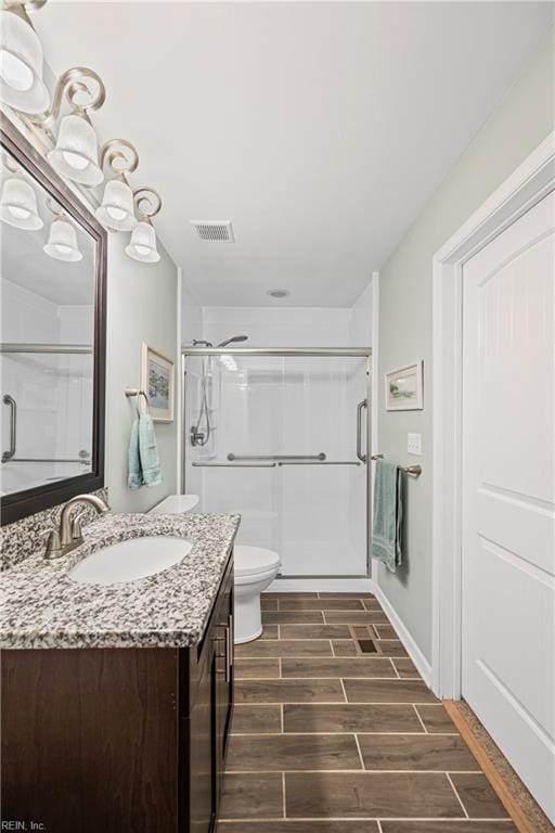 bathroom with visible vents, wood tiled floor, toilet, a stall shower, and vanity