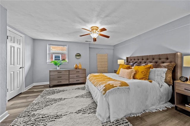 bedroom with ceiling fan, visible vents, baseboards, and wood finished floors