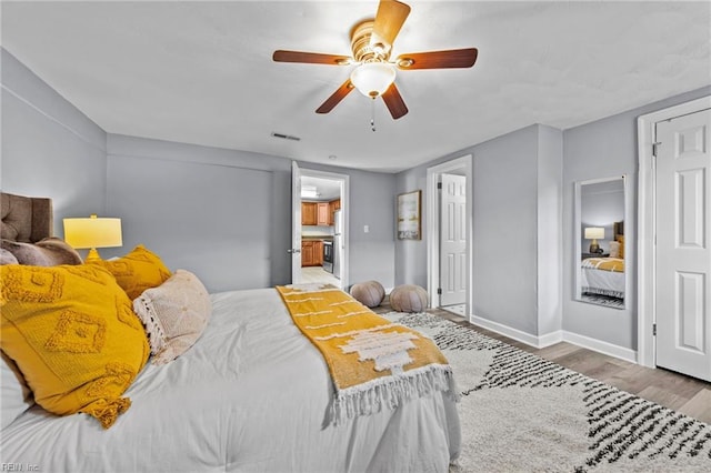 bedroom with a ceiling fan, wood finished floors, visible vents, and baseboards