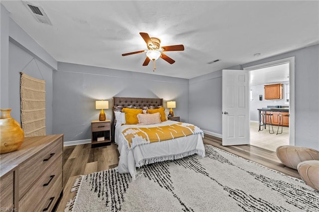 bedroom with a ceiling fan, wood finished floors, visible vents, and baseboards