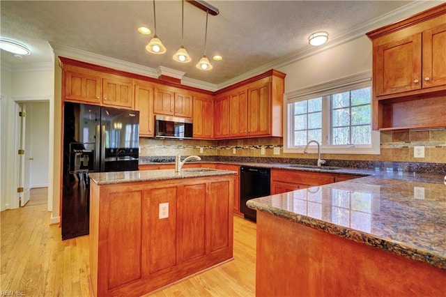 kitchen featuring black appliances, brown cabinetry, a kitchen island with sink, and a sink