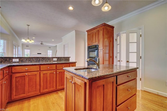 kitchen featuring a sink, light wood-style floors, dark stone countertops, and dobule oven black