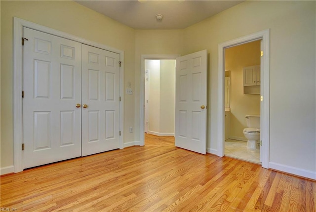 unfurnished bedroom featuring a closet, baseboards, ensuite bath, and light wood-style flooring