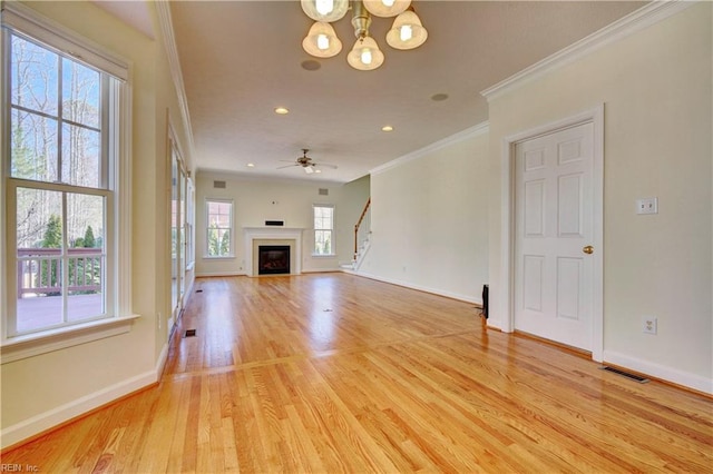 unfurnished living room featuring light wood-type flooring, visible vents, a glass covered fireplace, crown molding, and baseboards