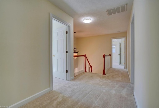 hallway featuring an upstairs landing, visible vents, carpet flooring, and baseboards