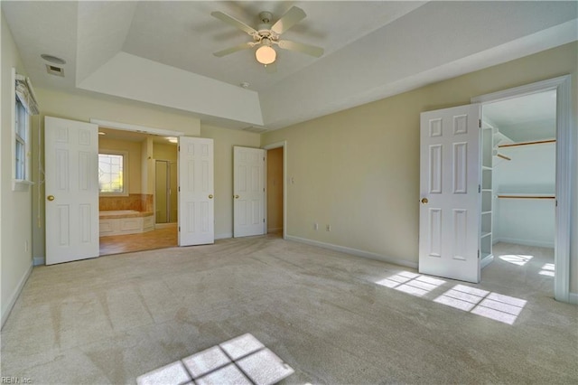 unfurnished bedroom featuring a tray ceiling, carpet, baseboards, and ensuite bathroom