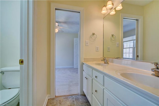 bathroom featuring double vanity, toilet, baseboards, and a sink