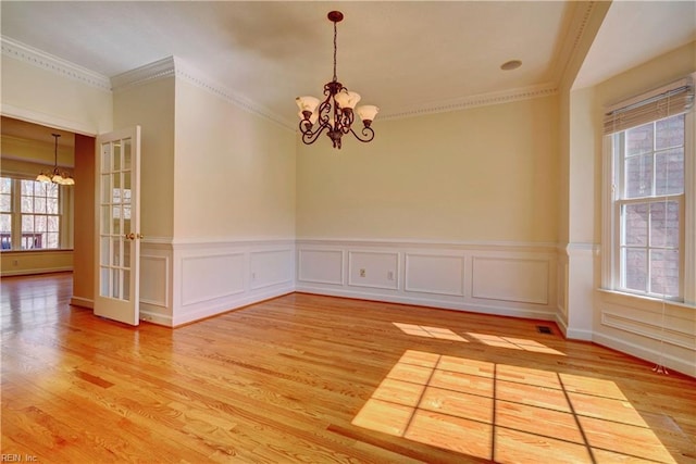 empty room featuring light wood-style flooring, a chandelier, wainscoting, and ornamental molding