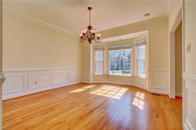 interior space with light wood-type flooring, visible vents, a notable chandelier, ornamental molding, and a decorative wall