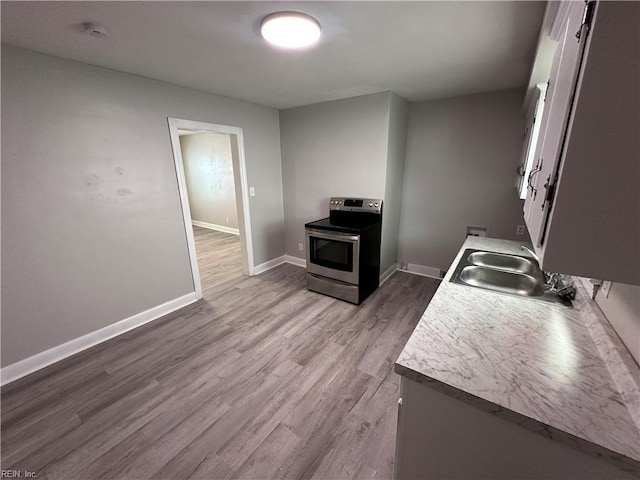 kitchen featuring wood finished floors, baseboards, electric range, a sink, and light countertops