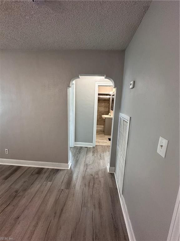 corridor with wood finished floors, visible vents, baseboards, arched walkways, and a textured ceiling