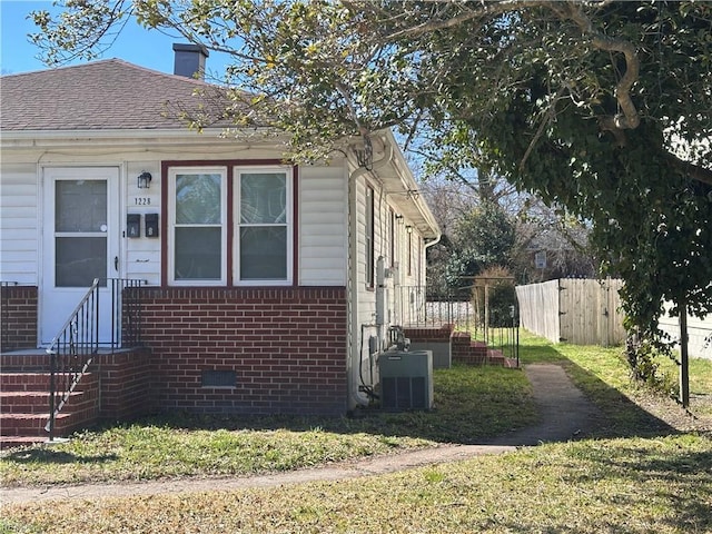 view of property exterior with fence, cooling unit, roof with shingles, brick siding, and a chimney