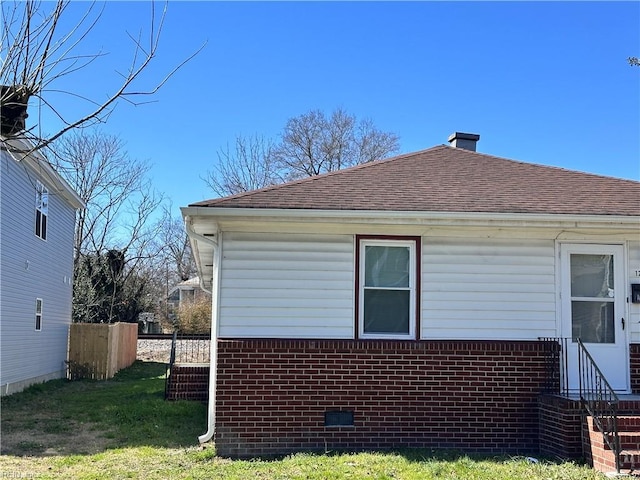 view of side of home with a shingled roof, a lawn, brick siding, and crawl space