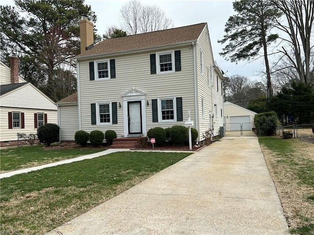 colonial house featuring a detached garage, a front lawn, fence, a chimney, and an outdoor structure