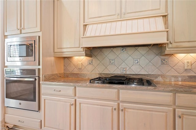 kitchen featuring decorative backsplash, custom range hood, light stone counters, and appliances with stainless steel finishes