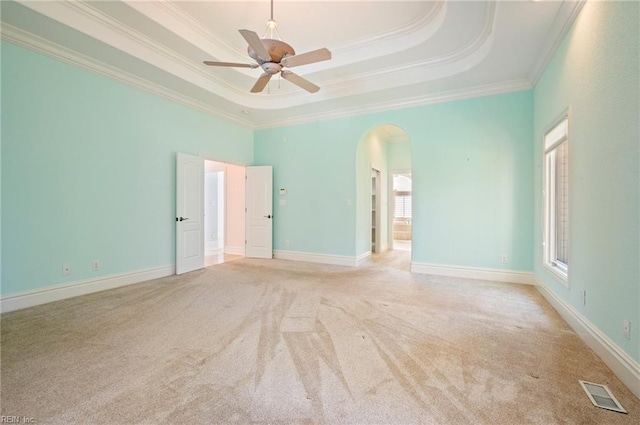 carpeted spare room with a tray ceiling, visible vents, arched walkways, and a ceiling fan