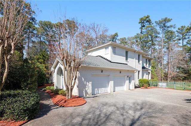 view of side of property with a garage, brick siding, driveway, and fence