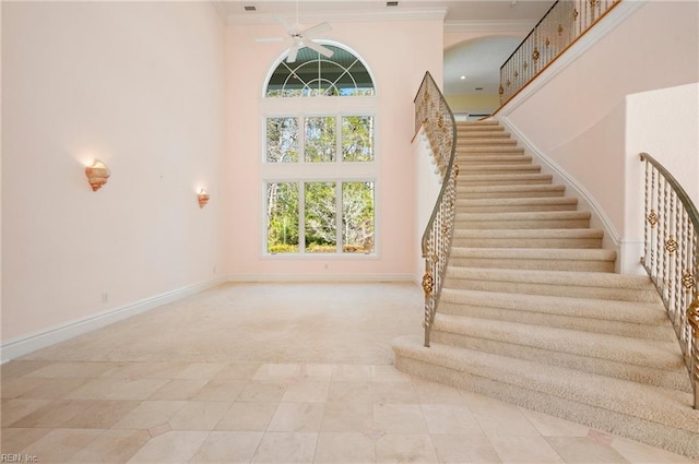 staircase featuring carpet, baseboards, a high ceiling, ornamental molding, and ceiling fan