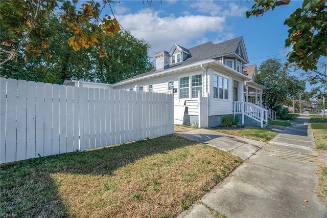 view of side of property featuring a lawn, a chimney, and fence