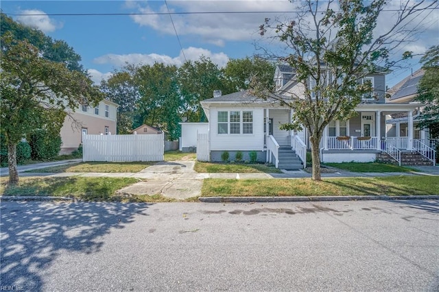 view of front facade with covered porch, a front yard, and fence