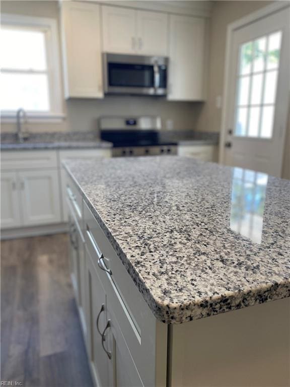 kitchen with light stone counters, a kitchen island, dark wood finished floors, stainless steel appliances, and white cabinets