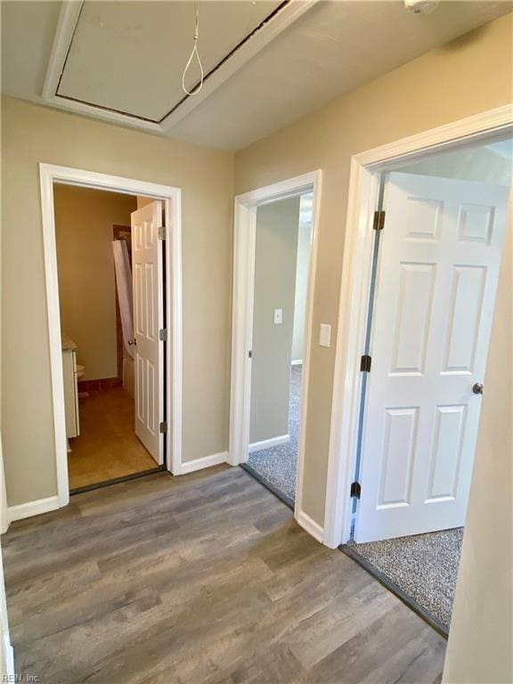 hallway featuring baseboards, attic access, and wood finished floors