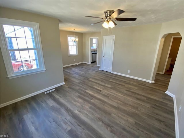 unfurnished living room with arched walkways, ceiling fan with notable chandelier, dark wood-type flooring, and baseboards