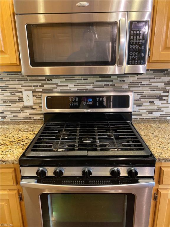 interior details with light brown cabinetry, backsplash, stainless steel appliances, and light stone countertops