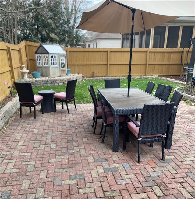 view of patio / terrace featuring outdoor dining space, an outbuilding, a fenced backyard, and a shed