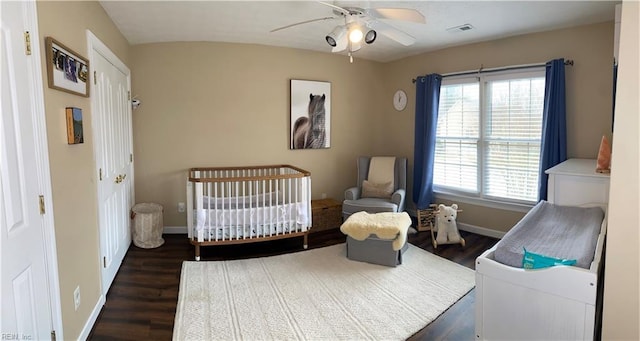 bedroom with wood finished floors, visible vents, baseboards, ceiling fan, and a crib