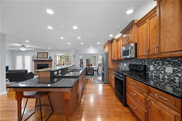 kitchen with an island with sink, appliances with stainless steel finishes, a kitchen breakfast bar, brown cabinetry, and a sink