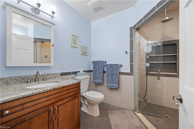 bathroom with tile patterned flooring, a shower stall, toilet, vanity, and tile walls