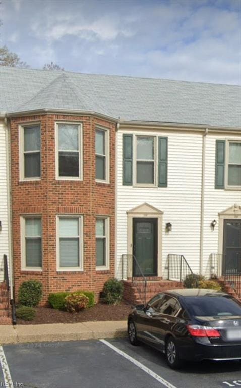 view of property featuring uncovered parking, brick siding, and a shingled roof