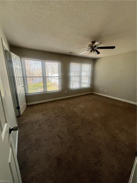 spare room with a ceiling fan, baseboards, dark colored carpet, and a textured ceiling