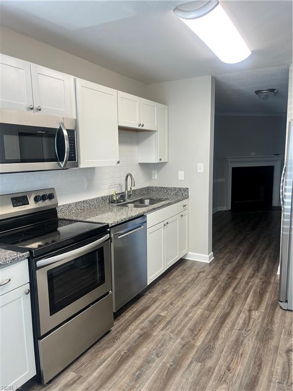 kitchen with a sink, backsplash, appliances with stainless steel finishes, and dark wood-style floors