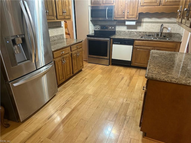 kitchen with brown cabinets, light wood-style flooring, a sink, tasteful backsplash, and appliances with stainless steel finishes