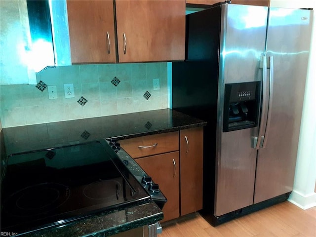 kitchen featuring decorative backsplash, dark stone countertops, stainless steel fridge, and light wood finished floors