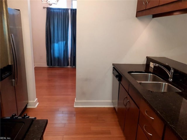 kitchen with light wood-style flooring, a sink, dark stone counters, appliances with stainless steel finishes, and baseboards